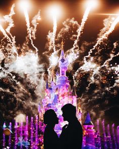 two people standing in front of a castle with fireworks