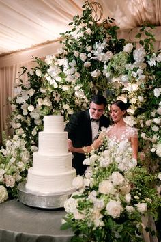 a bride and groom cutting their wedding cake together in front of an arch of flowers