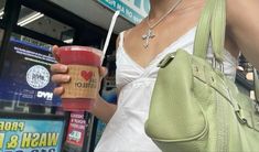 a woman holding a drink in her right hand and wearing a green purse on the other