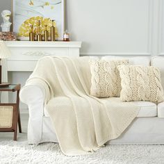 a living room with a white couch covered in a knitted blanket next to a fireplace