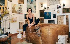 a woman sitting on top of a brown couch in a living room filled with pictures