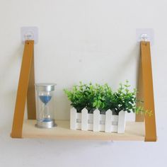 two wooden shelves with plants and an hourglass on them, one shelf has three small white boxes