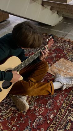 a young man sitting on the floor playing an acoustic guitar