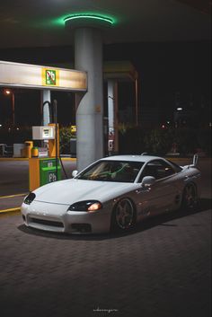 a white sports car parked in front of a gas station at night with its lights on