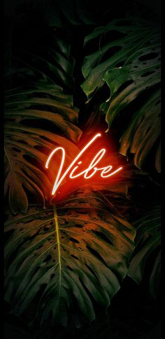 a neon sign that reads vie on it's side in front of some green leaves