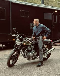 a man standing next to his motorcycle in front of a train car and black trailer