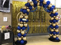 an arch made out of balloons and blue and gold balls in front of a party backdrop