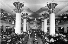 an old photo of people sitting at desks in a large room with columns on the ceiling