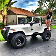 a woman standing on the hood of a white jeep parked in front of a house