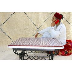 a man sitting at a table talking on a cell phone while wearing a red hat