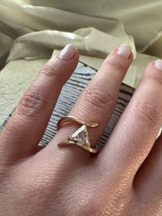 a woman's hand wearing a gold ring with a triangle shaped diamond on it