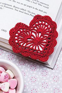 there is a bowl of candy next to a book and a heart - shaped doily