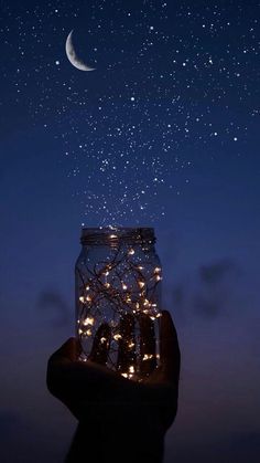 someone is holding up a jar with lights in it and the stars are falling out