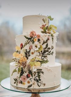 a three tiered cake with flowers on it sitting on top of a glass plate