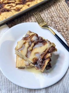 a white plate topped with cake next to a pan filled with cinnamon roll desserts