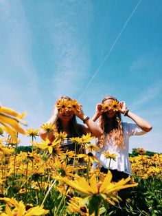 two girls standing in a field with sunflowers covering their eyes