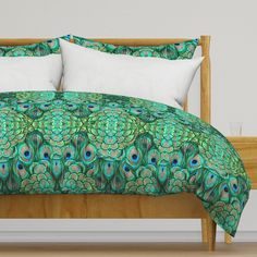 a bed with green and blue peacock feathers on it's comforter, along with two pillows