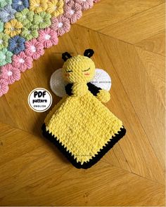 a crocheted yellow and black blanket with a bee on it sitting on a wooden floor