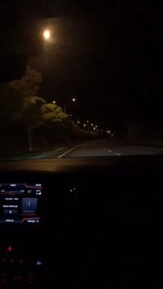 the dashboard of a car at night with street lights and trees on both sides of the road