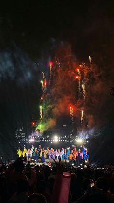 fireworks are lit up in the night sky as people stand on stage with their backs to the crowd