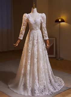 a white wedding dress on display in a room with a lamp and window behind it