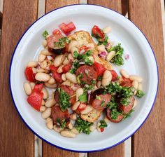 a white plate topped with beans, tomatoes and broccoli on top of a wooden table