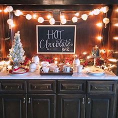 a buffet table with christmas decorations and lights on the wall behind it, along with a chalkboard sign that says hot chocolate bar