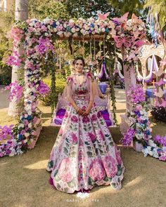 a woman in a wedding dress standing under a flower covered arbor with flowers all over it