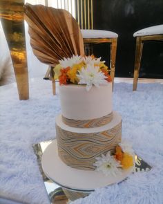 a three tiered wedding cake with white and orange flowers on the top, sitting on a blue tablecloth