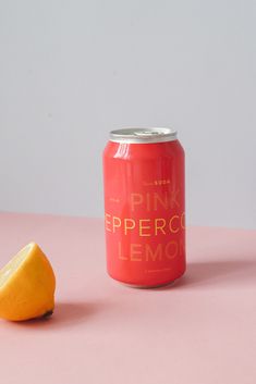 a can of pink pepper lemonade next to an orange slice on a pink surface