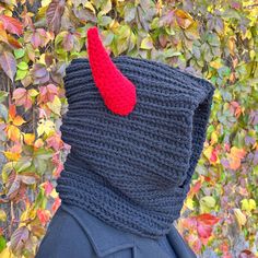 a person wearing a knitted mask with a red horn on it's head