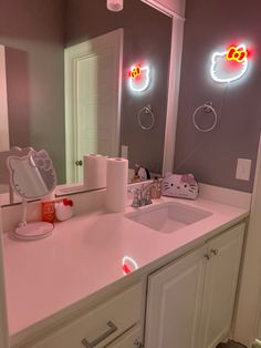 a pink bathroom with hello kitty lights on the wall and mirror above the sink area