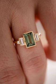 a woman's hand holding a ring with an emerald and baguette stone