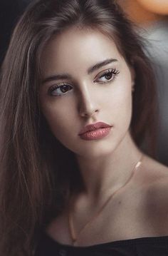 a woman with long brown hair wearing a black top and gold necklace is looking at the camera