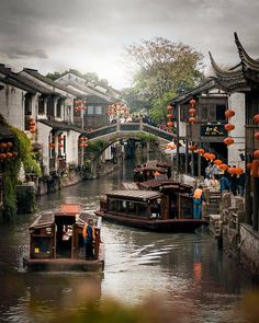 two boats traveling down a river next to buildings with orange lanterns hanging from the roof