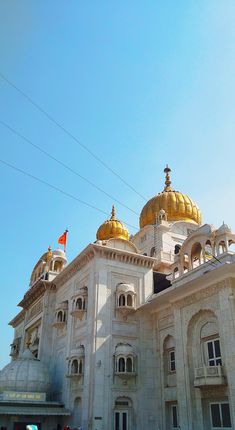 a large white building with gold domes on it's roof and two flags flying in the air