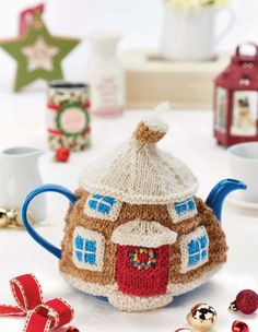 a knitted tea pot with a house on it next to christmas decorations and other items