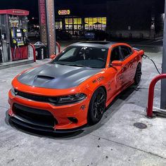 an orange dodge charger parked in front of a gas station