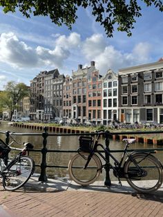 two bikes parked next to each other on the side of a bridge over water with buildings in the background