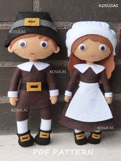 two stuffed dolls are standing next to each other in front of a brick wall, one is wearing a brown and white dress