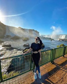 a woman standing next to a metal fence near the water and waterfall in niagara falls