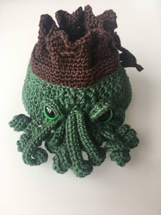 a crocheted green and brown hat with an octopus head on the front, sitting on a white surface