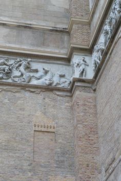 a clock on the side of a building with statues above it and below that is a brick wall