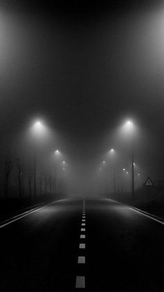 an empty road with street lights on both sides in the dark foggy night sky