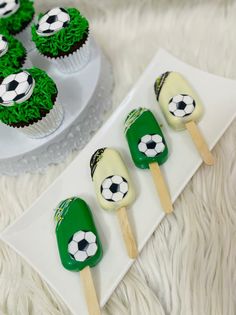 four cupcakes with soccer themed frosting and green icing are on a white plate