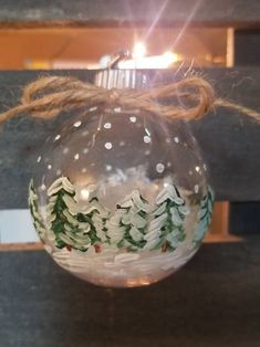 a glass ornament hanging from a string with pine trees on it and snow flakes