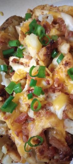 a white plate topped with cheesy potatoes covered in cheese and green onions on top