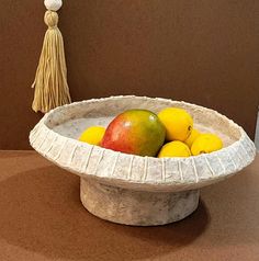 a white bowl filled with fruit next to a tasselled object on a table