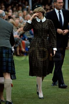 a woman in a dress and hat walking on the grass with other people behind her