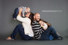 a man and woman holding a baby while sitting on the ground with their arms around each other